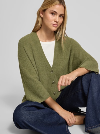 Kobiece model prezentuje Oversized Cardigan aus Baumwoll-Anteil Modell 'DAMSVILLE' od American Vintage, elastyczna mieszanka materiałów z bawełną, krój oversized fit, imitacja dzianiny, listwa guzikowa, dekolt w serek, długość tyłu w rozmiarze XS/S: 63 cm, długość rękawów w rozmiarze XS/S: 35 cm, całe ciało z przodu.