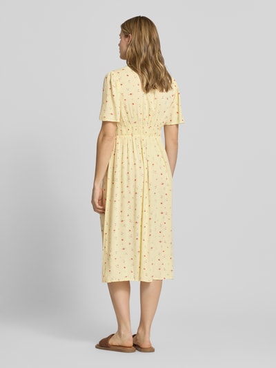 Modelka kobieca nosi A-Linien Midikleid aus reiner Viskose Modell 'TALA' od Pieces, jasny żółty, wzór allover, długość midi, krótki rękaw, gumka w talii, prosty dół, widok całej sylwetki od tyłu.