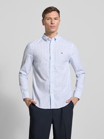 Männermodel draagt Regular Fit Vrijetijdsoverhemd uit katoenpopeline van Tommy Hilfiger met all-over streepmotief, rompkleur lichtblauw en wit, logo-stitching, button-downkraag, lange mouwen, afgeronde rompzoom, vooraanzicht bovenlichaam.