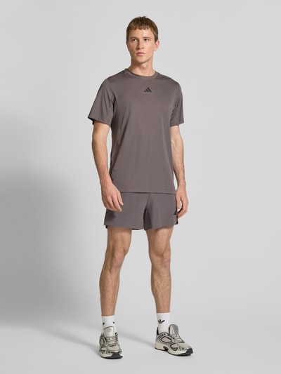 Mężczyzna model nosi Regular Fit Sport-Shorts mit elastischem Bund von adidas Training, efekt: jednolity kolor, krój regular fit, nadruk z logo, wstawka z siateczki, ściągacz: elastyczny, wpuszczane kieszenie, ganzkörperansicht von vorne.