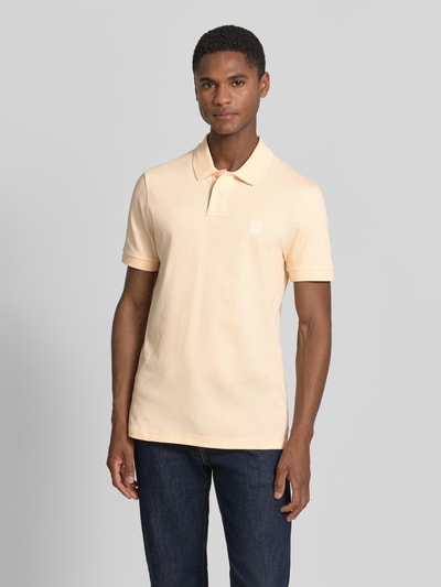Męski model nosi Slim Fit Poloshirt aus Baumwoll-Mix Modell 'PASSENGER' od BOSS Orange, efekt: jednolity kolor, naszywka z logo, kołnierzyk polo, zapięcie na 2 guziki, krótki rękaw, mieszanka bawełny, Ganzkörperansicht von vorne.