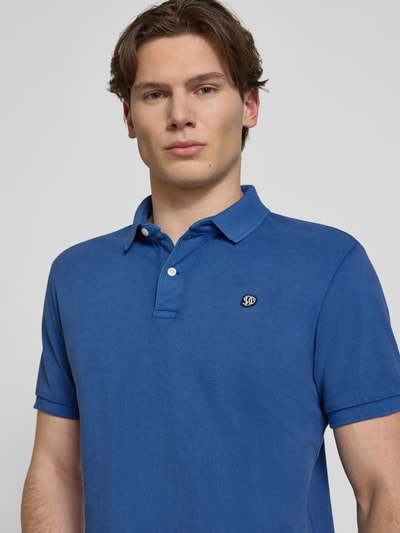 Männermodel trägt Regular Fit Poloshirt mit Logo-Stitching von Superdry in Blau, reine Baumwolle, Polokragen, Nahaufnahme Oberkörper.