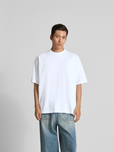 Männermodel trägt Oversized T-Shirt aus reiner Baumwolle von VETEMENTS in Weiß, mit Stehkragen, Label-Stitching, Ganzkörperansicht von vorne.