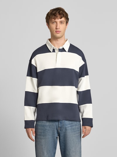 Männermodel trägt Sweatshirt mit Polokragen Modell 'UPSTATE' von Jack & Jones aus reiner Baumwolle im lockeren Schnitt, breite weiße und dunkelblaue Streifen, glatte Textur, Knopfleiste, überschnittene Schultern, Rückenlänge bei Größe M 68 cm, Ärmellänge 59 cm, Ganzkörperansicht von vorne.