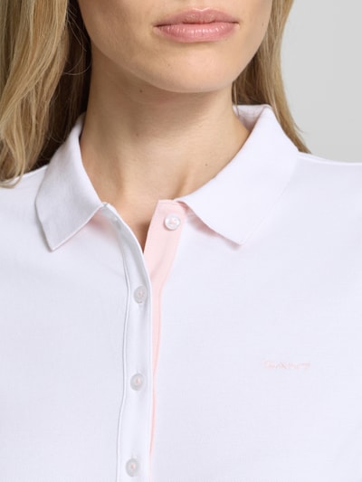 Frauenmodel trägt Slim Fit Poloshirt mit Label-Stitching von Gant aus Baumwoll-Elasthan-Mix, Knopfleiste, weiße Farbe, Nahaufnahme Oberkörper. Rückenlänge bei Größe S: 59 cm.