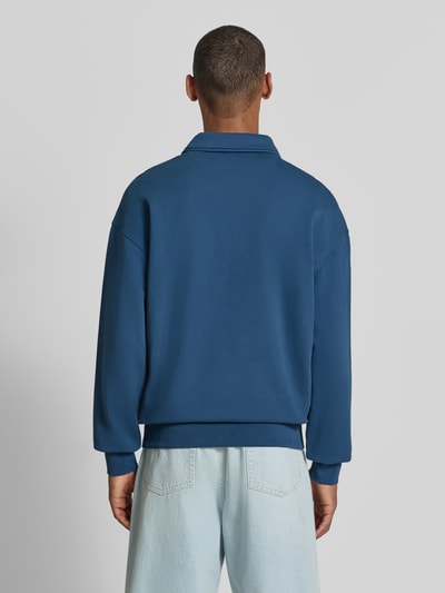Männermodel trägt Relaxed Fit Troyer aus reiner Baumwolle Modell 'ICONIC Å GMT' von ARMEDANGELS in Blau, Ganzkörperansicht Rückansicht.