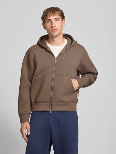 Männermodel trägt Relaxed Fit Sweatjacke mit Zweiwege-Reißverschluss von JACK & JONES in Braun, mit Känguru-Tasche und elastischen Abschlüssen, Ganzkörperansicht von vorne. Herren Sweatjacke, elastischer Material-Mix, Rückenlänge 65 cm, Ärmellänge 65 cm.