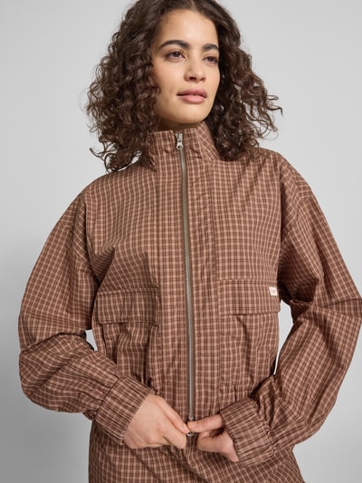 Kobiece modelka nosi Regular Fit Bomberjacke mit Logo-Patch Modell 'Zoe' von OH APRIL z bawełny, brązowy wzór w kratę, stójka, nakładane kieszenie, zamek błyskawiczny dwustronny, elastyczne wykończenia; długość tyłu w rozmiarze S: 51 cm, szerokość ramion w rozmiarze S: 56 cm, szerokość klatki piersiowej w rozmiarze S: 62 cm, długość rękawów w rozmiarze S: 56 cm; zdjęcie: zbliżenie górnej części ciała z przodu.