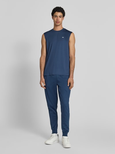 Męskimodel nosi top Relaxed Fit Top mit Logo-Print model 'OLIOS' od Ellesse, elastyczna mieszanka materiałów, okrągły dekolt, długość tyłu w rozmiarze M: 74 cm, granatowy kolor, gładka struktura, nadruk z logo, krój relaxed fit, Ganzkörperansicht von vorne.
