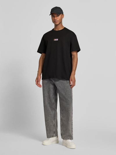 Męski model nosi T-Shirt mit Logo-Print Modell 'Chase' od Les Deux, czarny, bawełna, prosty krój, przód, zdjęcie całej sylwetki.