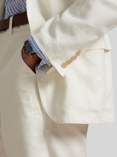 Mężczyzna nosi Regular Fit Anzugsakko aus reinem Leinen von Polo Ralph Lauren, jednokolorowy kremowy len, wyhaftowane logo, kieszeń z patką, widok zbliżony na bok.