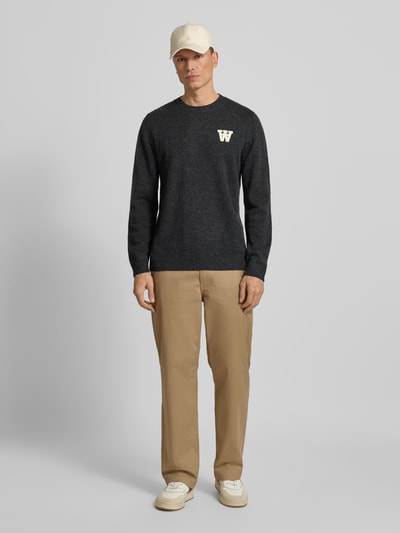 Männermodel trägt Strickpullover aus Lammwolle Modell 'Tay' von Wood Wood, dunkelgrau, Rundhalsausschnitt, Regular-Fit, Label-Stitching, Ganzkörperansicht von vorne. Kontext: Herren Strickpullover, Rückenlänge bei Größe M 72 cm, Ärmellänge 68 cm, reine Lammwolle.