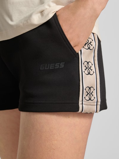 Vrouwenmodel draagt zwarte Shorts met Kordelzug en Logo-Print Modell 'BRITNEY' van Guess Activewear, loose fit, detailopname heup.