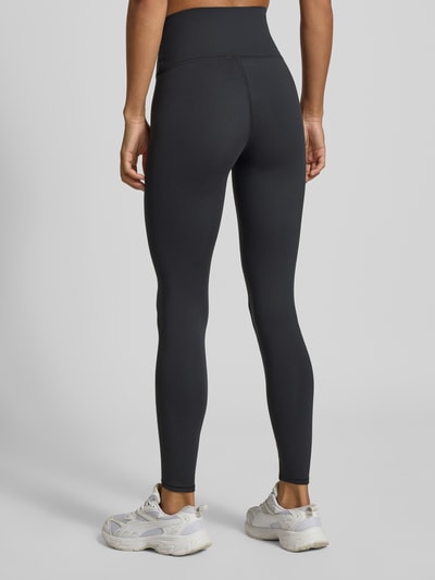 Frauenmodel trägt schwarze Leggings mit Label-Print Modell 'Harmony' von New Balance, schmale Passform, Ganzkörperansicht Rückansicht.