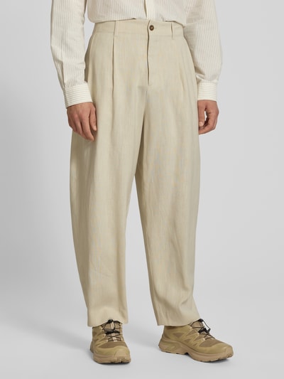 Männermodel trägt Stoffhose aus Viskose-Leinen-Mix von MAISON KITSUNÉ in Beige, Ballon-Schnitt, sichtbare Kellerfalten, Nahaufnahme Unterkörper, Eingrifftaschen, Knopf- und Reißverschluss.