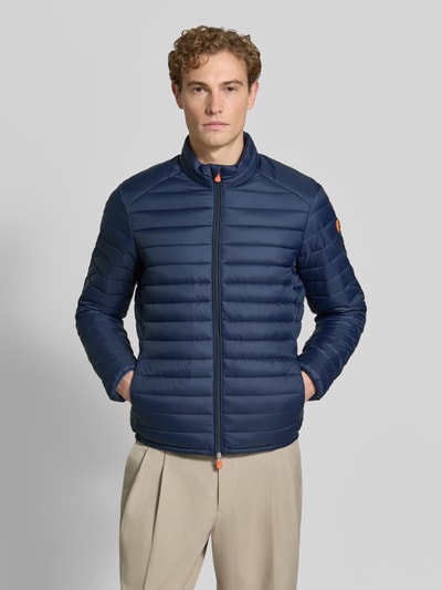 Männermodel trägt dunkelblaue Steppjacke mit Zweiwege-Reißverschluss Modell 'ALEXANDER' von Save The Duck, Slim Fit, Ganzkörperansicht von vorne. Herrenjacke mit Stehkragen, Reißverschlusstaschen, Rückenlänge 67 cm, Schulterbreite 47 cm, Brustweite 57 cm, Ärmellänge 68 cm.