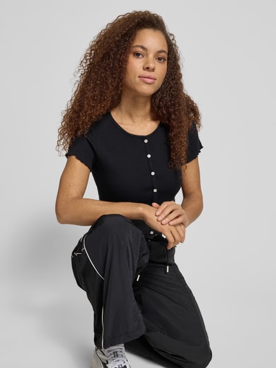 Młodzieżowy modelka nosi Slim Fit T-Shirt aus Baumwoll-Mix od Tommy Jeans, czarna, krój slim fit, logo-stitching, krótki rękaw, frill, ripp, u-boot, materiał bawełniany, jednolity kolor, ujęcie: półzbliżenie tułowia z przodu