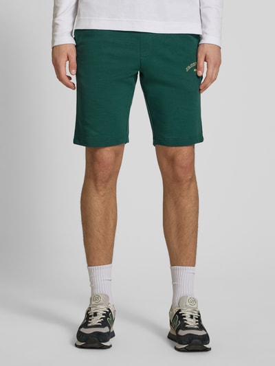 Männermodel trägt Shorts mit Logo-Print Modell 'GORDON' von Jack & Jones aus grünem Baumwoll-Mix, Relaxed-Fit, Nahaufnahme Oberschenkel frontal.