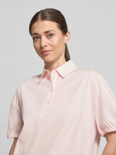 Kobiece model prezentuje Regular Fit Bluse mit Polokragen von Marc Cain, jasnoróżowa bluzka z bawełny, krótkie rękawy, elastyczne zakończenia rękawów, pas z tunelem; krój regular fit, długość tyłu 59 cm, długość rękawów 19 cm, widok na górną część ciała z przodu