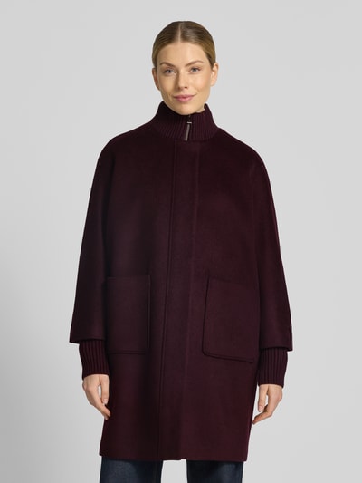 Frauenmodel trägt Mantel aus Woll-Mix mit gestricktem Stehkragen von COMMA, gerade Form, dunkles Bordeaux, große Taschen, Nahaufnahme Oberkörper. Rückenlänge 92 cm, Schulterbreite 40 cm, Brustweite 60 cm, Ärmellänge 63 cm, Viskose-Anteil, Reiß- und Druckknopfverschluss, gestrickte Ärmelabschlüsse.