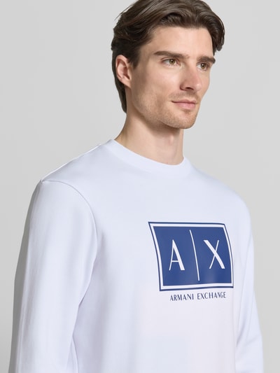 Męski model nosi Sweatshirt mit Logo-Print und Rundhalsausschnitt von ARMANI EXCHANGE, biała bawełna, krój loose fit, nadruk logo na przodzie, długość tyłu 65 cm, długość rękawa 61 cm, zbliżenie na górną część ciała.