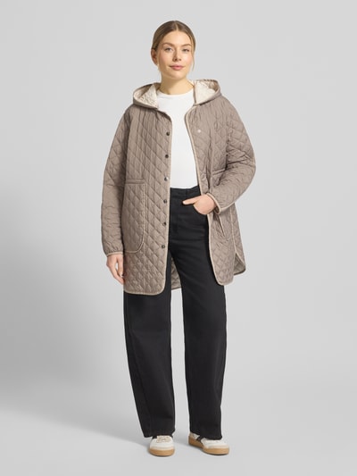 Modelka kobieca ma na sobie Steppmantel mit Druckknopfleiste od WHITE LABEL w kolorze beżowym, wyraźne pikowanie, luźny krój, z kapturem i naszywanymi kieszeniami, długość tyłu w rozmiarze 36: 74 cm, szerokość ramion w rozmiarze 36: 46 cm, szerokość w biuście w rozmiarze 36: 55 cm, długość rękawa w rozmiarze 36: 61 cm, ujęcie pełnej sylwetki od przodu