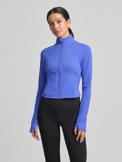 Modelka kobieca nosi Slim Fit Jacke mit Stehkragen Modell 'Storm' od Fabletics w kolorze niebieskim, krój slim fit, krótki fason, z pętelkami na kciuki; długość tyłu w rozmiarze S: 44 cm, szerokość ramion w rozmiarze S: 36 cm, szerokość w biuście w rozmiarze S: 42 cm, długość rękawa w rozmiarze S: 74 cm, gładka tekstura, całkowity widok z przodu