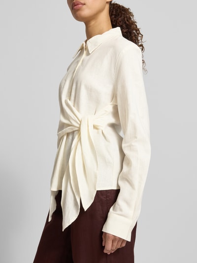 Frauenmodel trägt Bluse aus Leinen-Viskose-Mix mit Knoten-Detail von GUIDO MARIA KRETSCHMER WOMAN, taillierter Schnitt, Hemdblusenkragen, Knopfleiste, Modell MATHILDA, cremefarben, strukturierte Oberfläche, Ganzkörperansicht von vorne.