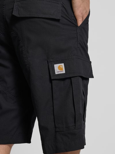 Mannenmodel draagt Shorts mit Cargotaschen van Carhartt Work In Progress in regular fit met cargozakken en achterzakken, zwart, detailopname rechterbeen.