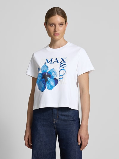 Frauenmodel trägt weißes Boxy-Fit Damen T-Shirt aus reiner Baumwolle Modell 'MAMBO' von MAX&Co. mit großem blauen Blumenprint, Ganzkörperansicht von vorne.