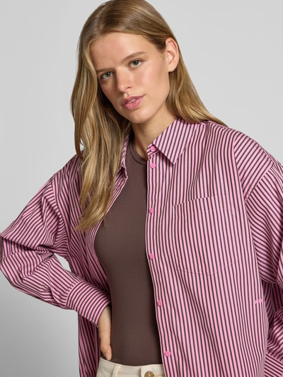 Frauenmodel trägt Relaxed Fit Hemdbluse aus reiner Baumwolle Modell 'JAMIE' von JJXX in Rosa mit schwarzen Streifen, Nahaufnahme Oberkörper. Hemdblusenkragen, langärmliges Design, aufgesetzte Brusttasche, durchgehende Knopfleiste, überschnittene Schultern, Rückenlänge 77 cm, Ärmellänge 56 cm, Baumwollstruktur.
