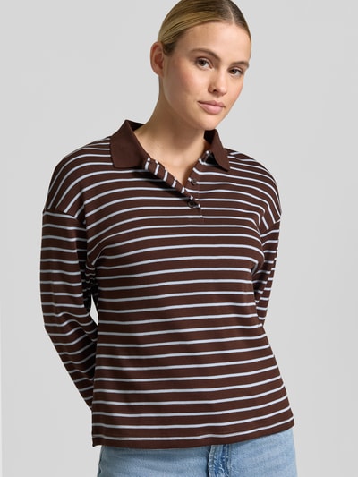 Frauenmodel trägt Relaxed Fit Poloshirt aus reiner Baumwolle Modell 'TIMOTHEE' von MANGO in Braun mit weißen Streifen, Langarm, Polokragen, strukturierte Baumwolloberfläche, Rückenlänge bei Größe S 60 cm, Ganzkörperansicht von vorne.