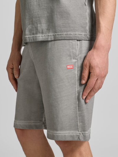 Männermodel trägt Sweatshorts aus reiner Baumwolle von Diesel in Grau mit Label-Print, Used-Look, lockerer Passform, Nahaufnahme Oberschenkel.