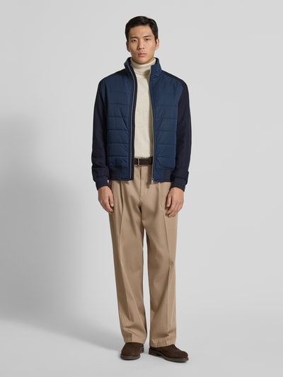 Männermodel trägt Jacke mit Stehkragen von Christian Berg Men in Blau, Regular-Fit, Reißverschluss, Reißverschlusstaschen, gerippte Abschlüsse; Rückenlänge 26 cm, Schulterbreite 19 cm, Brustweite 19 cm, Ärmellänge 26 cm; Ganzkörperansicht von vorne.