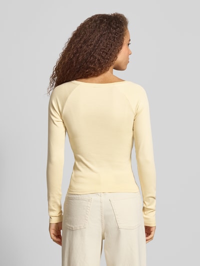 Modelka kobieca ma na sobie Slim Fit Longsleeve mit V-Ausschnitt von Gina Tricot z elastycznej mieszanki bawełny, krój slim fit, dekolt w serek, bluzka z długim rękawem, długość tyłu w rozmiarze S: 48 cm, jasny kolor, widok całej sylwetki z tyłu.