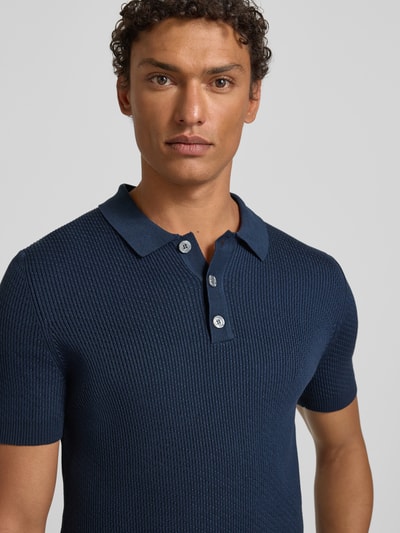 Männermodel trägt Slim Fit Poloshirt mit Strukturmuster von JOOP! Collection aus reiner Baumwolle, Knopfleiste, Label-Detail, Nahaufnahme Oberkörper.
