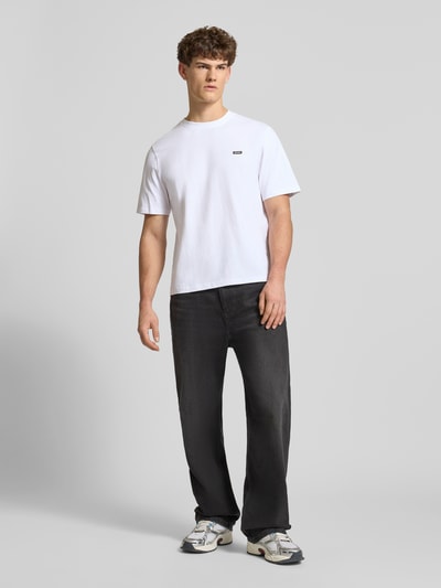 Männermodel trägt Basic T-Shirt mit kleinem Logo-Patch auf der Brust von REVIEW in Weiß, gerade geschnitten, reine Baumwolle, Ganzkörperansicht von vorne.