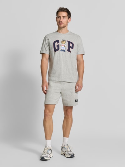 Männermodel trägt Straight Fit Shorts mit Logo-Stitching Modell 'Heritage' von GAP aus Baumwoll-Mix in Hellgrau, Ganzkörperansicht von vorne.