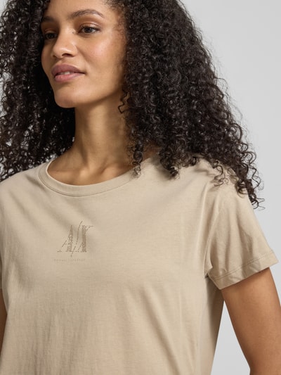Frauenmodel trägt T-Shirt aus reiner Baumwolle von Armani Exchange in Beige mit geradem Schnitt, Rundhalsausschnitt, Label-Detail, Strasssteinbesatz, Nahaufnahme Oberkörper.
