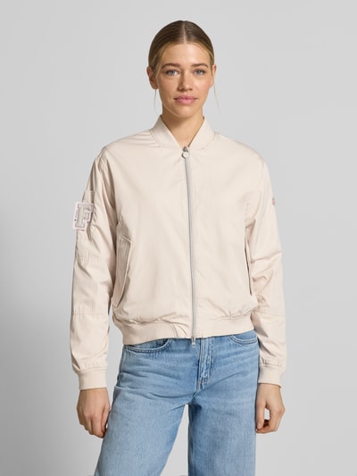 Frauenmodel trägt Bomberjacke mit Label-Patches Modell 'BROOKLYN NEO' von Frieda & Freddies in Beige, Gerader-Schnitt, Stehkragen, Zweiwege-Reißverschluss, Seitliche Pattentaschen mit Druckknopfverschluss, Gerippte-Abschlüsse; Rückenlänge 49 cm, Schulterbreite 42 cm, Brustweite 55 cm, Ärmellänge 63 cm; Ganzkörperansicht von vorne.