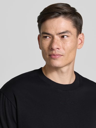 Männermodel trägt Relaxed Fit T-Shirt aus reiner Baumwolle von Marc O'Polo in Schwarz, unifarben, Label-Schriftzug, Nahaufnahme Oberkörper.