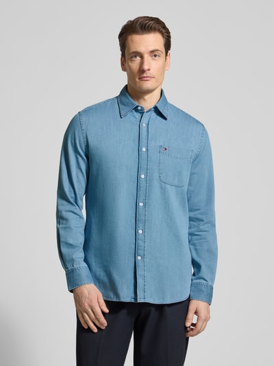 Männermodel trägt Regular Fit Jeanshemd aus reiner Baumwolle von Tommy Hilfiger in Denim-Optik mit Haifischkragen, Logo-Stitching, Ganzkörperansicht von vorne.