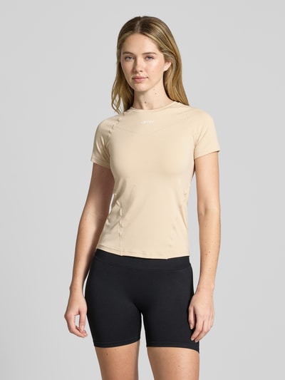 Modelka kobieca ma na sobie T-Shirt mit Rundhalsausschnitt und Logo von aim'n, beżowy, materiał z domieszką stretchu, krój slim fit, logo z przodu, długość pleców w rozmiarze S: 54 cm, widok całopostaciowy z przodu.