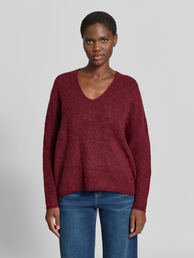Frauenmodel trägt Strickpullover aus Woll-Mix mit V-Ausschnitt Modell 'THORA' von MOS MOSH, rote Farbe, strukturierte Textur, Regular Fit, Nahaufnahme Oberkörper. Rückenlänge bei Größe S 82 cm, Ärmellänge 46 cm, Alpaka-Anteil.