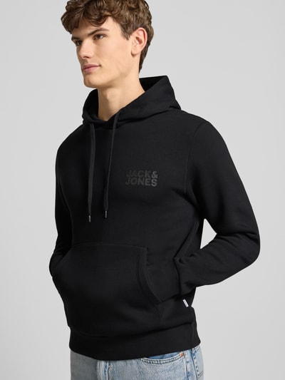 Männermodel trägt Hoodie mit Label-Print und Känguru-Tasche von Jack & Jones in Schwarz, Baumwoll-Mix, Regular Fit, Nahaufnahme Oberkörper.