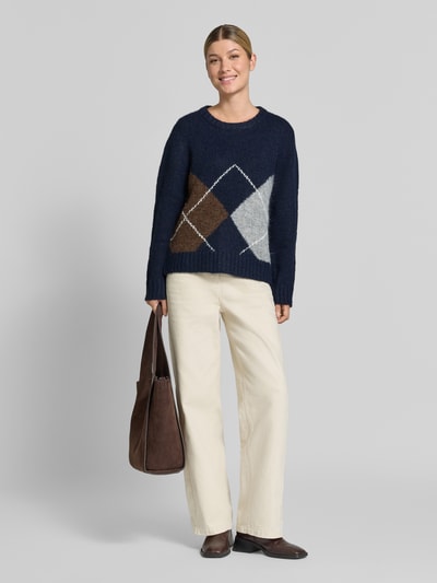 Frauenmodel trägt Strickpullover mit Woll-Anteil und Rundhalsausschnitt von ICHI, dunkle Rauten, beige Hose, Ganzkörperansicht von vorne. Modell 'BAYANA', Regular Fit, Rückenlänge 60 cm, Ärmellänge 70 cm.