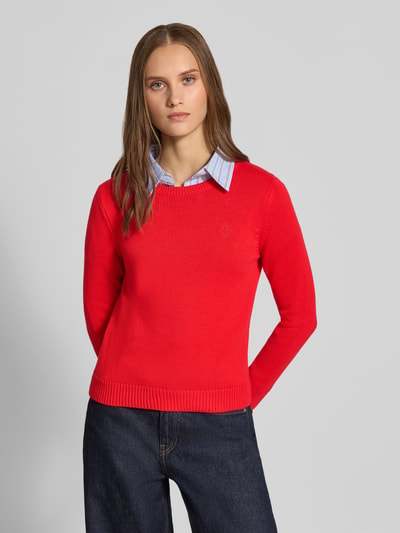 Frauenmodel trägt Slim Fit Pullover aus reiner Baumwolle von REVIEW in Rot mit Strick-Optik, Logo-Stitching, Ganzkörperansicht von vorne.