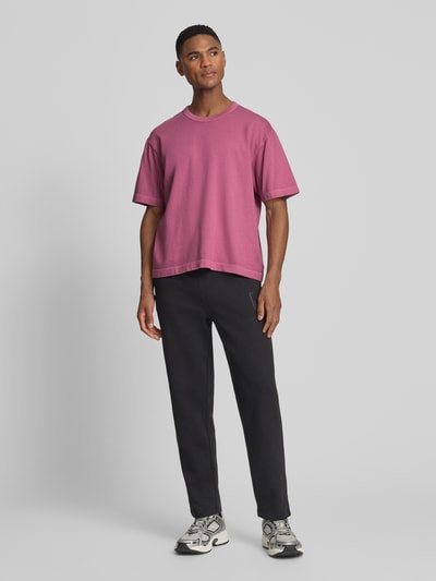 Männermodel trägt Cropped T-Shirt mit Rundhalsausschnitt von GAP in Pink, reine Baumwolle, kombiniert mit dunkler Hose, Ganzkörperansicht von vorne.