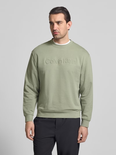 Männermodel trägt Sweatshirt mit Rundhalsausschnitt und Logo von CK Calvin Klein in Grün, Baumwoll-Elasthan-Mix, Regular-Fit, Ganzkörperansicht von vorne. Rückenlänge bei Größe M: 68 cm, Ärmellänge: 60 cm.