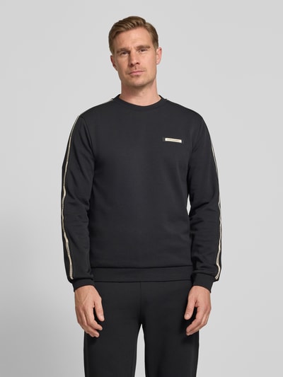 Männermodel trägt Sweatshirt mit Label-Details und Rundhalsausschnitt von EA7 Emporio Armani in Schwarz, Baumwoll-Mix, Regular-Fit, Ganzkörperansicht von vorne. Rückenlänge 63 cm, Ärmellänge 66 cm, dezente strukturierte Oberfläche.